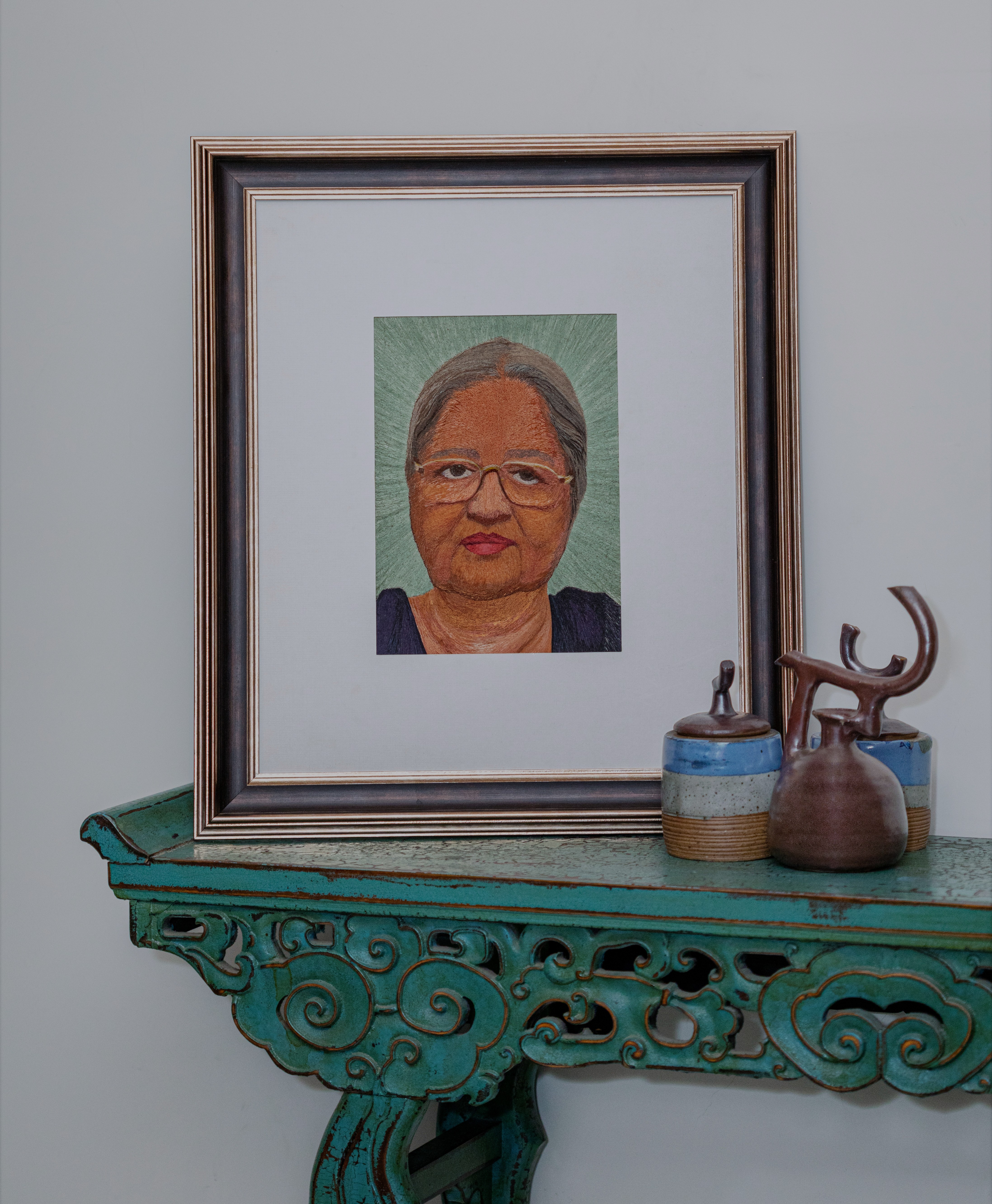 The subject is an 80 year-old woman in her reading glasses. The transparency of reading glasses and grey tones of the hair in embroidery showcases how ageing comes with its own grace
The greys in skin tones have been offset by a deep blue and aqua green background.